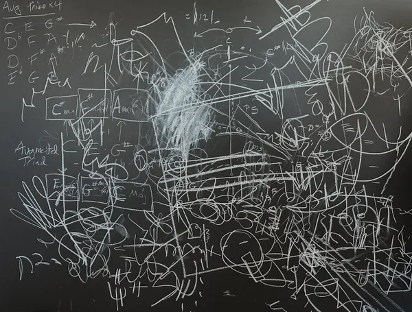Chalk on a blackboard: dense white scribbles and circles among written musical note names and chord diagrams